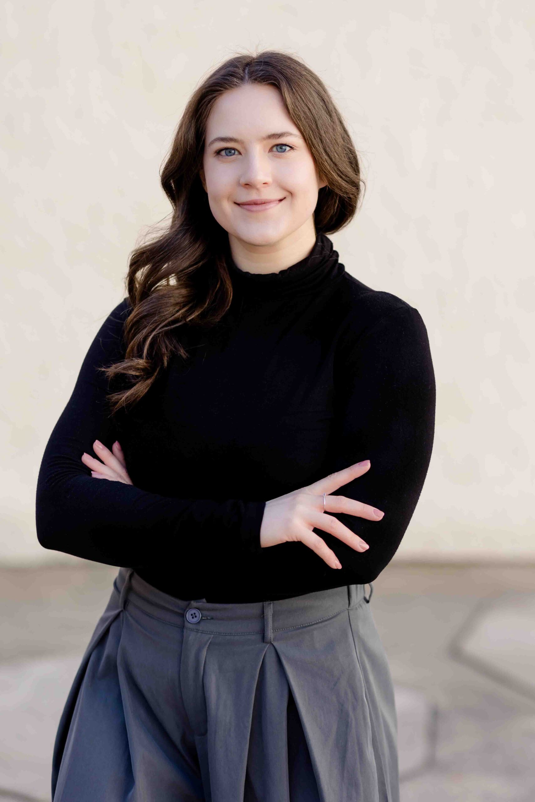 Authentisches Bewerbungsfoto einer jungen Frau mit leichtem Lächeln, verschränkten Armen, schwarzem Oberteil und neutralem Hintergrund – professionell und natürlich aufgenommen - Bewerbungsfotos Freiberg