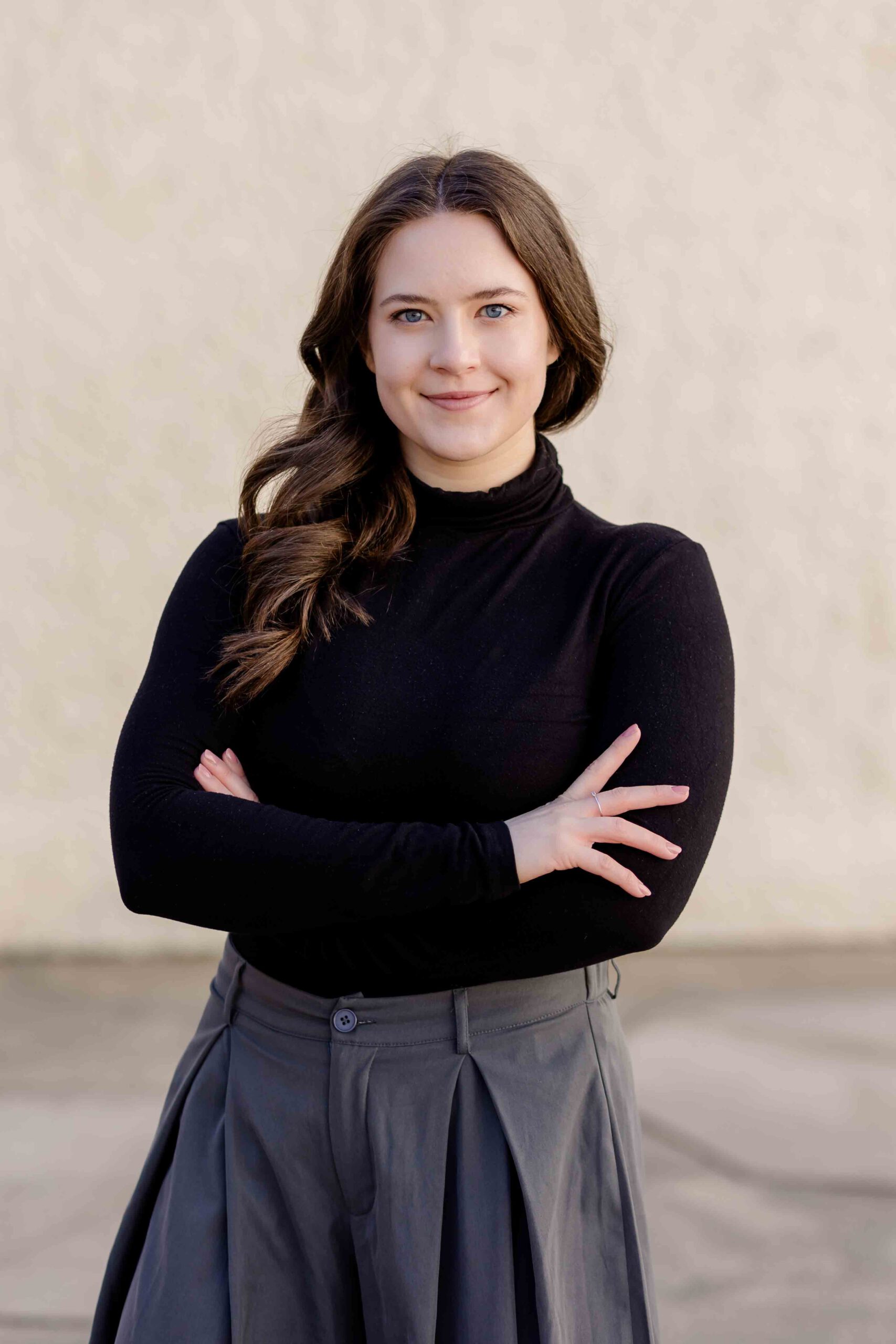 Authentisches Bewerbungsfoto einer jungen Frau mit leichtem Lächeln, verschränkten Armen, schwarzem Oberteil und neutralem Hintergrund – professionell und natürlich aufgenommen - Bewerbungsfotos Freiberg