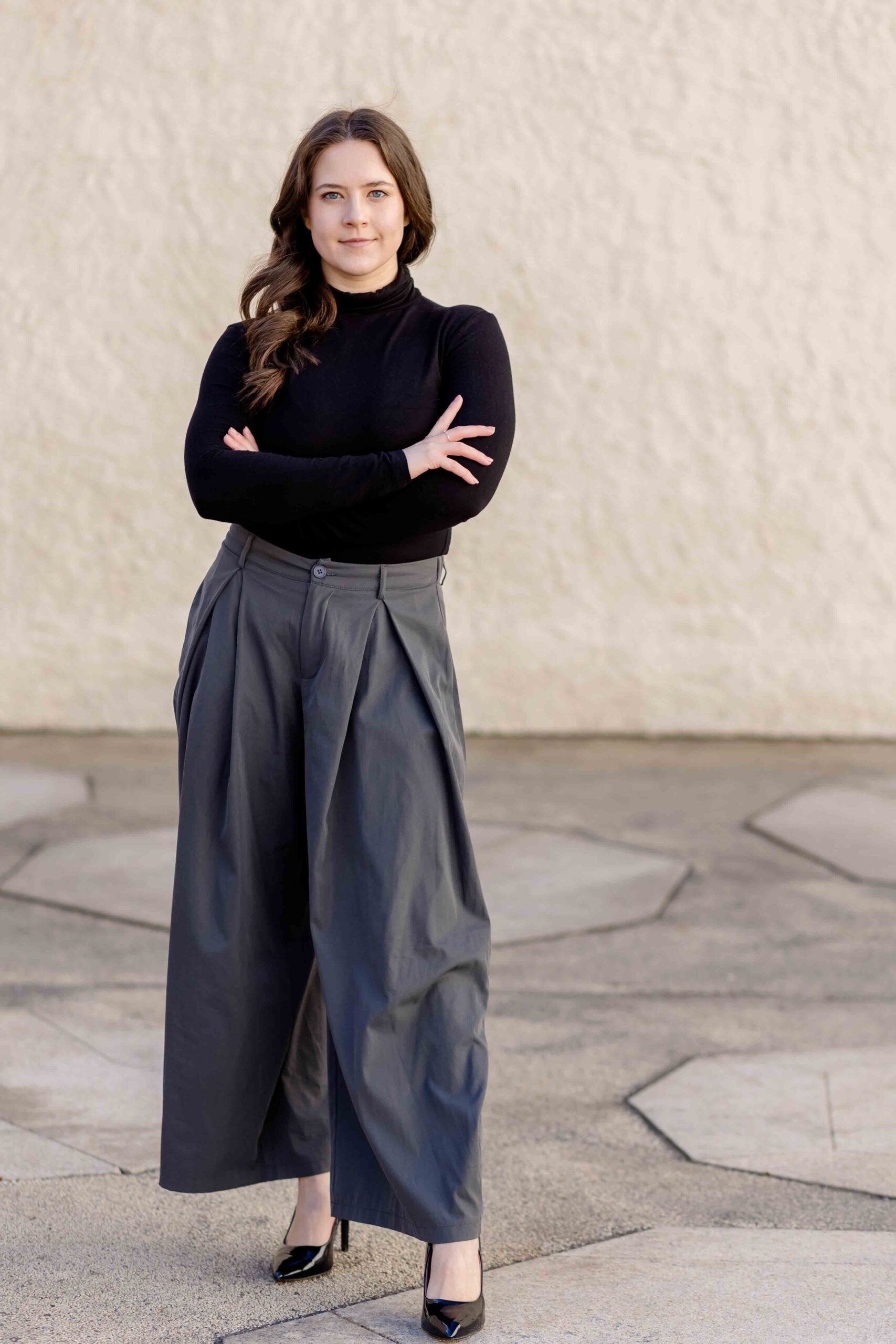 Authentisches Bewerbungsfoto einer jungen Frau mit leichtem Lächeln, verschränkten Armen, schwarzem Oberteil und neutralem Hintergrund – professionell und natürlich aufgenommen - Bewerbung Freiberg