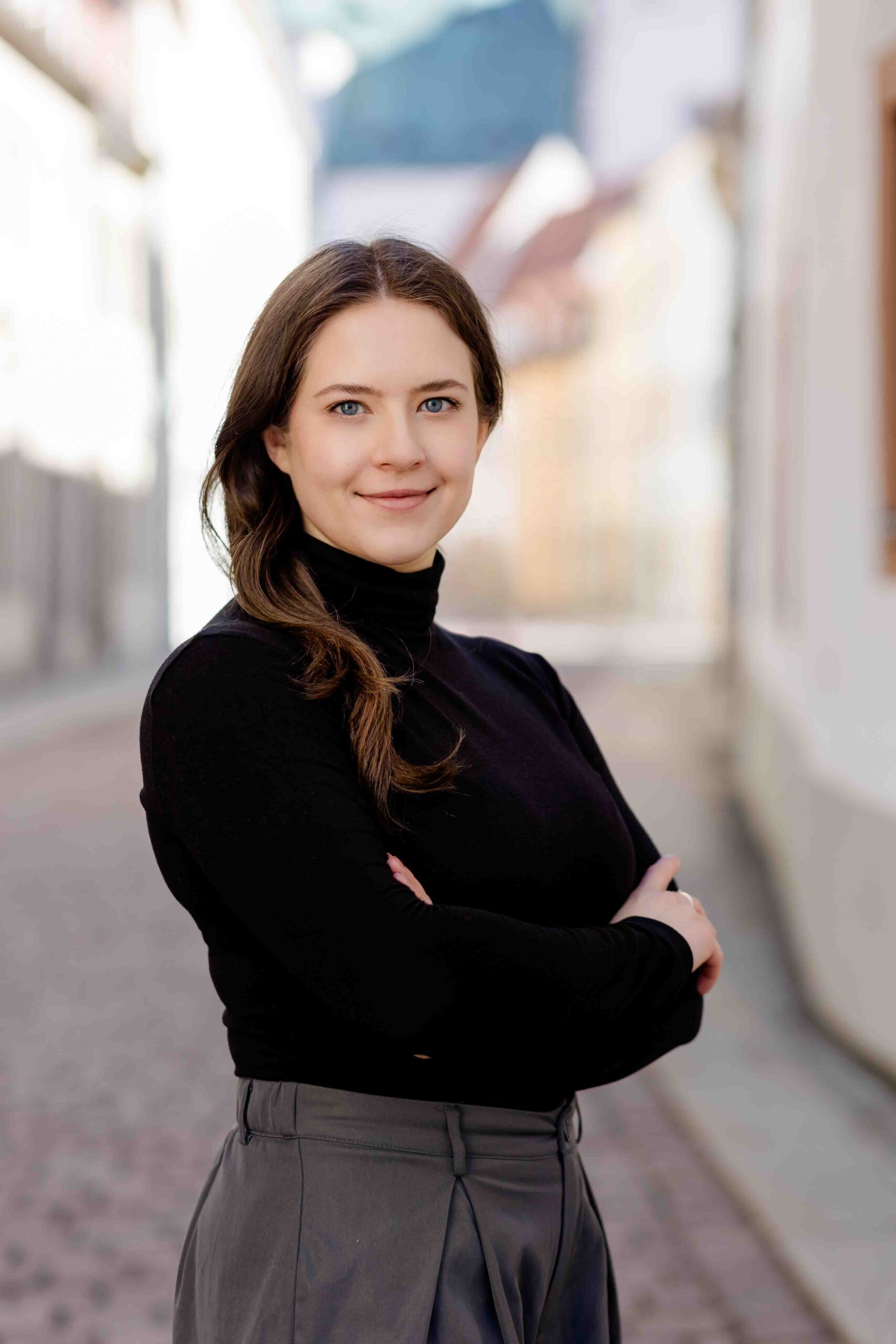 Authentisches Bewerbungsfoto einer jungen Frau mit leichtem Lächeln, verschränkten Armen, schwarzem Oberteil und neutralem Hintergrund – professionell und natürlich aufgenommen - Bewerbungsfotos Freiberg - Freiberg - Bewerbung