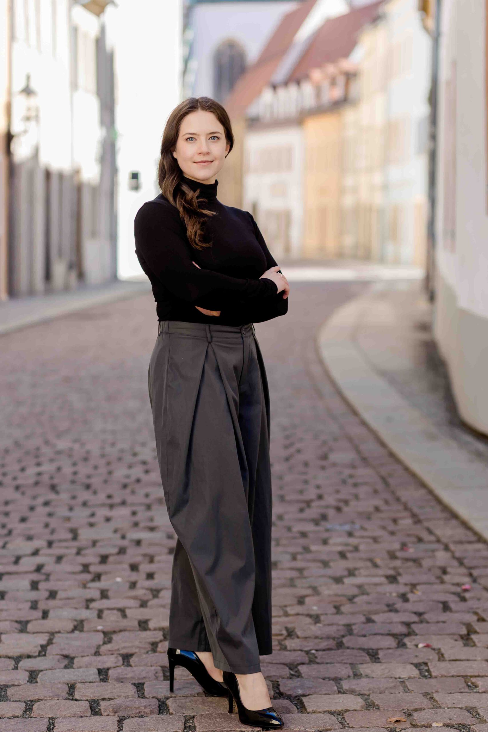 Authentisches Bewerbungsfoto einer jungen Frau mit leichtem Lächeln, verschränkten Armen, schwarzem Oberteil und neutralem Hintergrund – professionell und natürlich aufgenommen - Bewerbungsfotos Freiberg