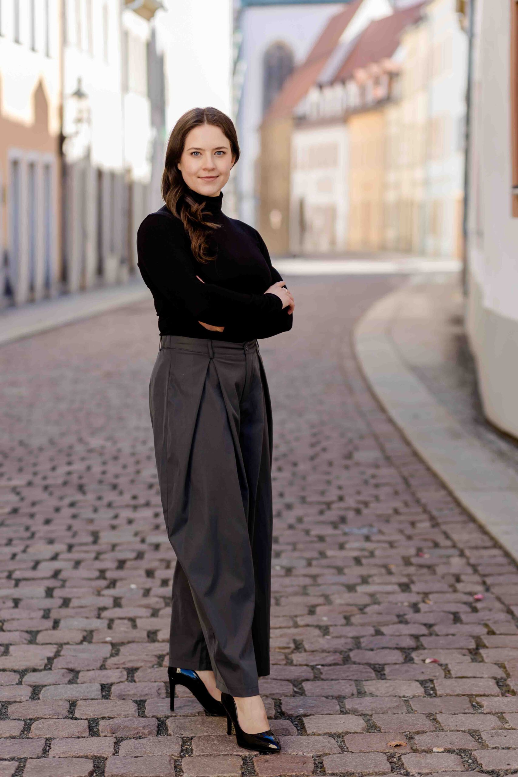 Authentisches Bewerbungsfoto einer jungen Frau mit leichtem Lächeln, verschränkten Armen, schwarzem Oberteil und neutralem Hintergrund – professionell und natürlich aufgenommen - Bewerbungsfotos Freiberg - Bewerbungsbilder