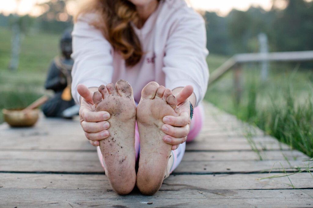 Businessfotos Yoga: Detailaufnahme von schmutzigen Füßen beim Yoga auf einem Holzsteg in der Natur – natürlich und ungezwungen