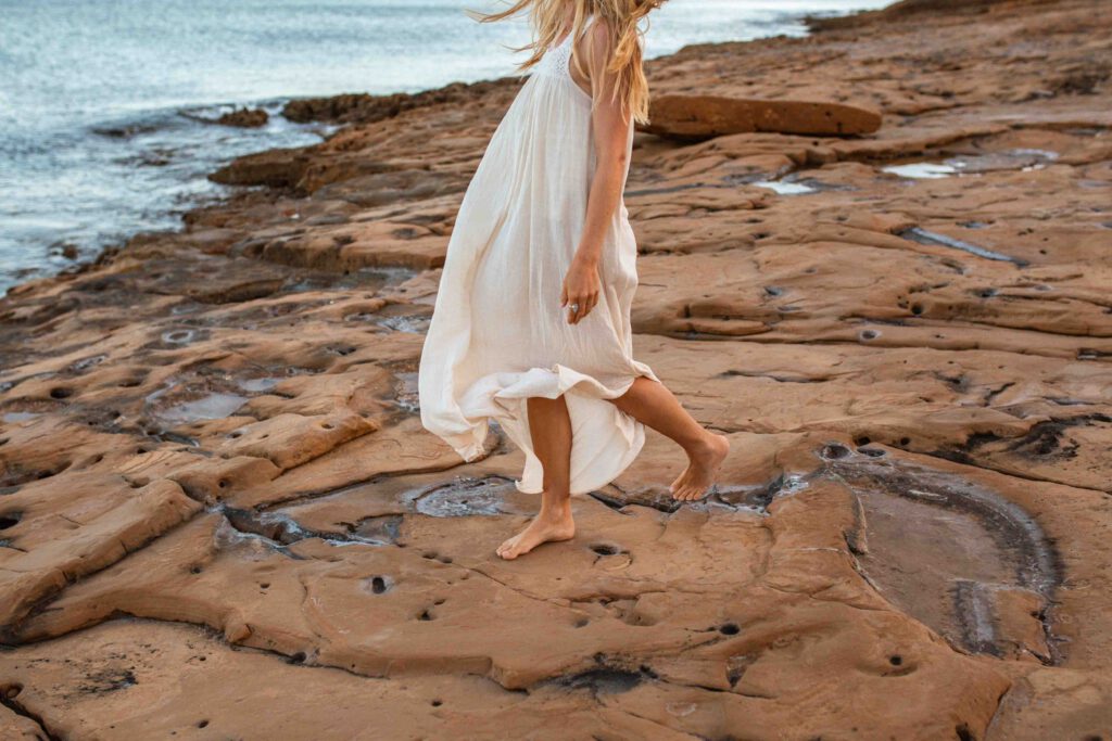 Frau im weißen Kleid am Steinstrand