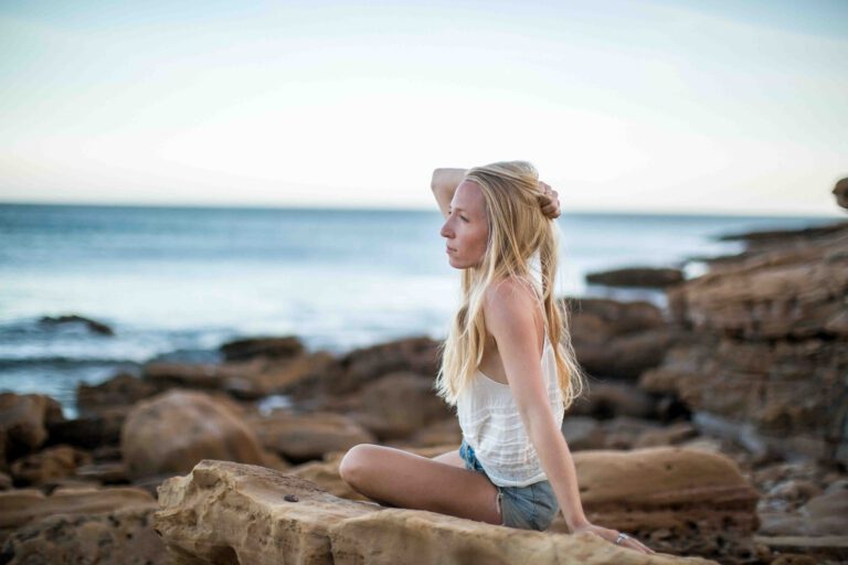 Frau im weißen Kleid sitzt auf Stein am Steinstrand